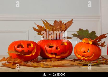 Drei geschnitzte Halloween-Kürbisse mit Herbstblättern auf einem Tisch Stockfoto