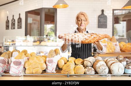 Bäckerin, die in einer Bäckerei einen großen Laib frisch gebackenes Brot hält Stockfoto