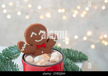 Ein Lebkuchenmann sitzt in einem roten Becher mit Marshmallows. Der Becher ist von Weihnachtsdekorationen umgeben, darunter ein Baumzweig und ein Haufen Re Stockfoto