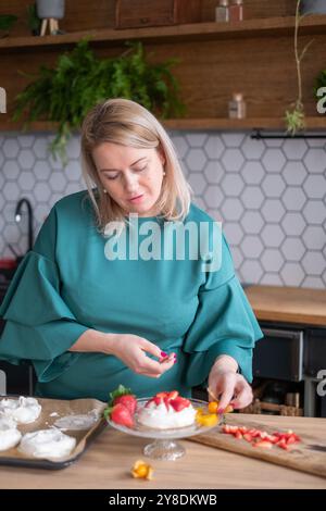 Dame, die Pavlova mit Erdbeeren in der modernen Küche dekoriert, kulinarische Kreativität nach Hause, Dessertzubereitungskonzept Stockfoto