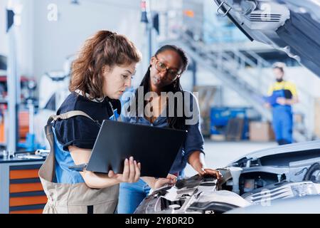 Mechaniker im Kfz-Service bestellt einen neuen Motor für beschädigtes Fahrzeug mit Laptop. Mitarbeiter neben dem Kunden, der online nach Komponenten sucht, um alte Komponenten in einem defekten Fahrzeug zu ersetzen Stockfoto