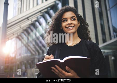 Selbstständige Unternehmerin mit gemischter Rasse, die in ihrem Notizbuch schreibt Stockfoto