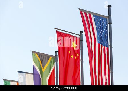 Verschiedene Nationalflaggen fliegen auf Fahnenmasten vor blauem Himmel, chinesische Flagge, amerikanische Flagge Stockfoto