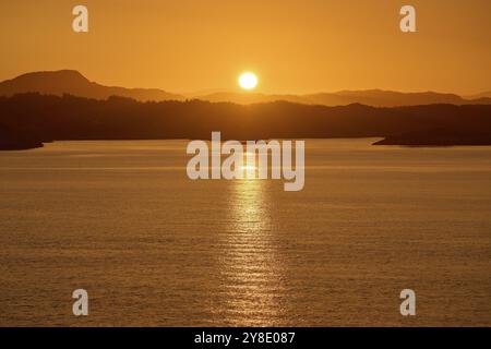 Ein sanfter oranger Sonnenaufgang hinter den dunklen Silhouetten der Berge und eines ruhigen Meeres, Herbst, Bergen, Nordsee, Norwegen, Europa Stockfoto