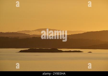 Ein sanfter oranger Sonnenaufgang hinter den dunklen Silhouetten der Berge und eines ruhigen Meeres, Herbst, Bergen, Nordsee, Norwegen, Europa Stockfoto