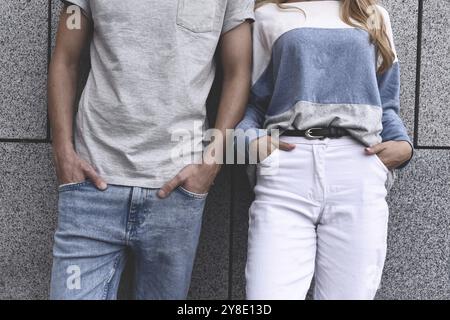 Zwei Freunde, die sich an eine Wand lehnen und einander ignorieren, ein Mann und eine Frau mit grauem Hintergrund Stockfoto