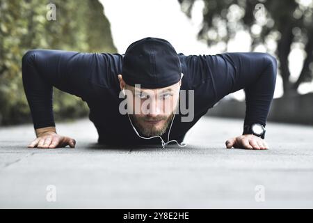Junge bärtige Sportler trainieren in einem Park und machen eine Reihe von Liegestützen im Freien Stockfoto