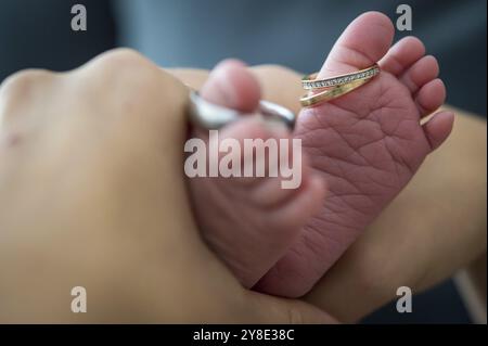 Nahaufnahme von Babyfüßen, die von den Händen gehalten werden, mit goldenen Ringen an einem Zeh Stockfoto