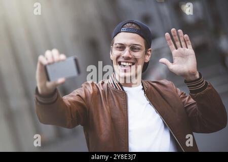 Selfie-Manie der junge Mann macht Selfie mit der Kamera. Er trägt lässige, trendige Kleidung und einen Schnappverschluss Stockfoto