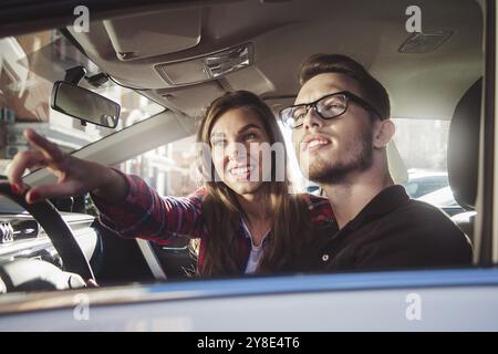 Viel Spaß beim Reisen. Schönes junges Paar, das auf den Beifahrersitzen sitzt und lächelt, während ein hübscher Mann ein Auto fährt Stockfoto