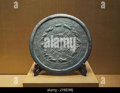 Ein alter chinesischer Bronzespiegel mit aufwändigen Schnitzereien von Tieren und Symbolen ist an einem Stand in einem Museum ausgestellt Stockfoto