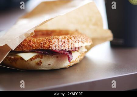 Ein köstlicher, herzhafter Sesam Bagel, hoch gestapelt mit Käse und Schinken, der auf einem Tisch liegt Stockfoto