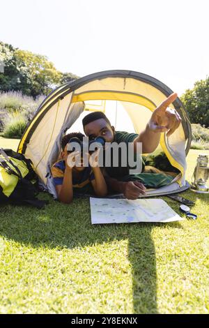Glücklicher afroamerikanischer Vater und Sohn, der im Zelt liegt und durch ein Fernglas im Garten blickt Stockfoto
