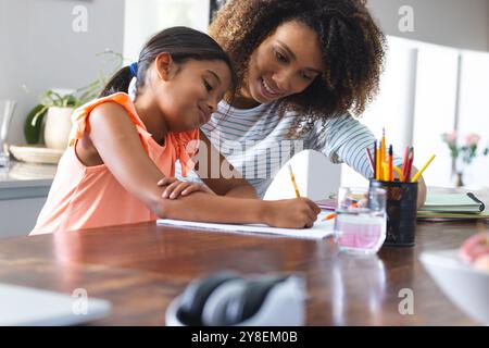 Die birassische Mutter hilft einer jungen birassischen Tochter bei Hausaufgaben zu Hause Stockfoto