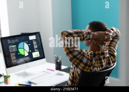 Ansicht von Hinten Nahaufnahme eines jungen afrikanischen amerikanischen Mann an einem Schreibtisch mit den Händen hinter seinem Kopf auf einem Monitor im modernen Büro sitzen Stockfoto