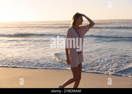 Wunderschöne kaukasische Frau, die während des Sonnenuntergangs am Strand spaziert und genießt Stockfoto