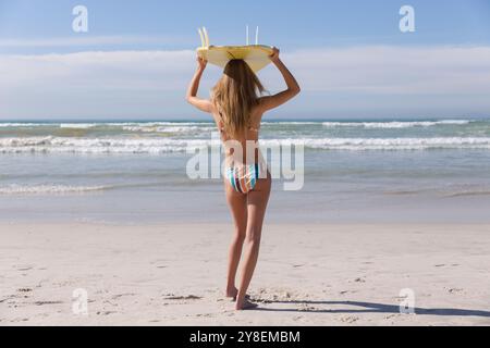 Weiße Frau im Bikini mit Surfbrett auf dem Kopf am Strand Stockfoto