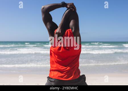 Rückansicht eines afroamerikanischen Mannes, der sich am Strand ausdehnt Stockfoto