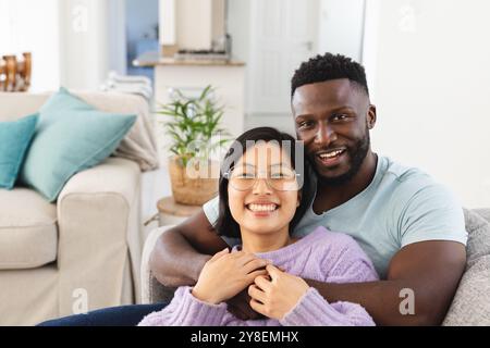 Porträt eines glücklichen, vielfältigen Paares, das auf Sofa sitzt und sich umhüllt Stockfoto