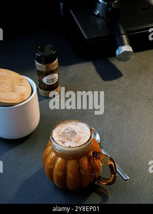 Eine Tasse Kürbis Pie Gewürz Latte Kaffee auf grauem Tisch, Kaffeemaschine im Hintergrund Stockfoto