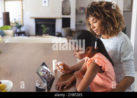 Birassische Mutter hilft einer birassischen Tochter mit Medikamenten zu Hause Stockfoto