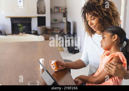 Birassische Mutter hilft einer jungen birassischen Tochter mit Medikamenten zu Hause mit Kopierraum Stockfoto