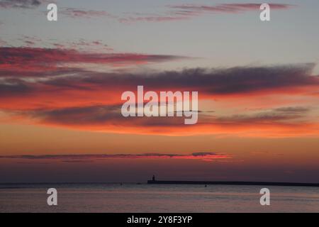 Die Sonne beginnt hinter dem Leuchtturm von South Shields an der Nordostküste aufzugehen, dessen oberste Kuppel vor kurzem ersetzt wurde, nachdem er von Storm Babet getroffen wurde. Bilddatum: Samstag, 5. Oktober 2024. Stockfoto