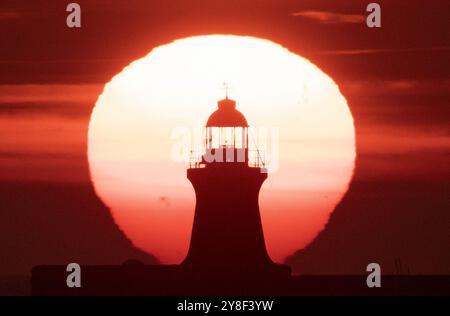 Die Sonne beginnt hinter dem Leuchtturm von South Shields an der Nordostküste aufzugehen, dessen oberste Kuppel vor kurzem ersetzt wurde, nachdem er von Storm Babet getroffen wurde. Bilddatum: Samstag, 5. Oktober 2024. Stockfoto