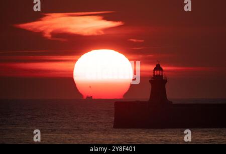 Die Sonne beginnt hinter dem Leuchtturm von South Shields an der Nordostküste aufzugehen, dessen oberste Kuppel vor kurzem ersetzt wurde, nachdem er von Storm Babet getroffen wurde. Bilddatum: Samstag, 5. Oktober 2024. Stockfoto