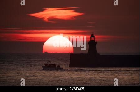 Die Sonne beginnt hinter dem Leuchtturm von South Shields an der Nordostküste aufzugehen, dessen oberste Kuppel vor kurzem ersetzt wurde, nachdem er von Storm Babet getroffen wurde. Bilddatum: Samstag, 5. Oktober 2024. Stockfoto