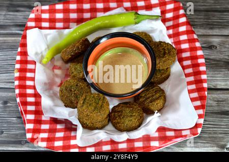 Traditionelle ägyptische frittierte Falafelbällchen mit Tahini und grünem Pfeffer serviert auf einem Teller, grüner Burger, hergestellt aus gemahlenen Kichererbsen und breiten Bohnen, tief Stockfoto