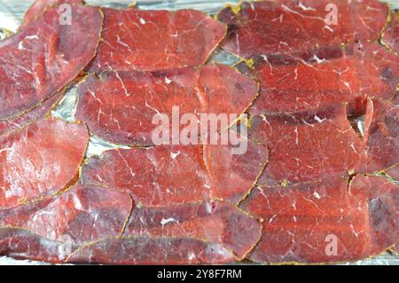 Dünne Scheiben Rindfleisch-Pastrami, aus Rinderbrust hergestellt, rohes Fleisch wird gebraten, teilweise getrocknet, mit Kräutern und Gewürzen gewürzt, dann geräuchert und gedünstet, li Stockfoto