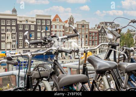 Niederlande. Verschiedene Fahrräder auf einem Fahrradparkplatz vor dem Hintergrund typischer Vintage-Gebäudefassaden in Amsterdam Stockfoto