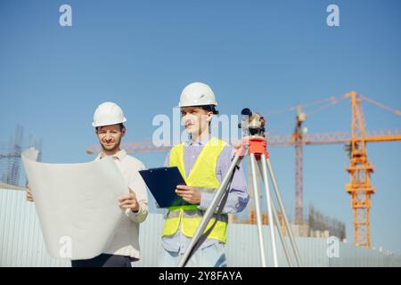 Team von Bauexperten, die mit Surveyor Level auf der neuen Baustelle Zeichnungen erstellen Stockfoto