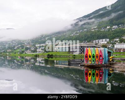 Aus nächster Nähe sehen Sie farbenfrohe Kajaks, die sich auf friedlichem Seewasser spiegeln, nebelige norwegische Berglandschaft am Morgen. Stockfoto