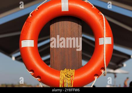 Orangefarbener Rettungsring mit einem Seil, das an einem hölzernen Pier-Zaun an der Küste hängt, Rettungsboje für Seeverkehrssicherheit Stockfoto