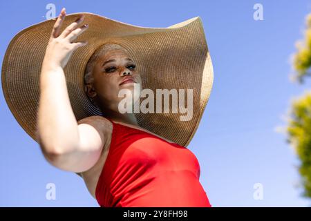 Unverändertes Porträt glücklicher birassischer Frau in großem Sonnenhut und rotem Badeanzug im sonnigen Garten Stockfoto