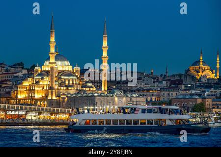 Turkiye. Istanbul. Eine Fähre fährt vor der Yeni Cami Moschee bei Einbruch der Dunkelheit Stockfoto