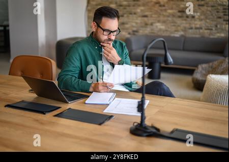 Ängstlicher junger Geschäftsmann mit Hand am Kinn, der Finanzberichte analysiert, während er am Schreibtisch im Büro arbeitet Stockfoto