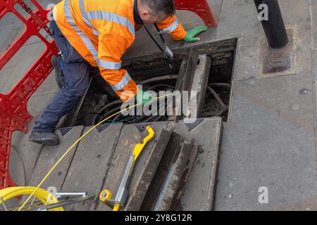 Ein Techniker im Bereich Telefonie oder Kommunikation steckt neue Kabel in ein Loch in der Straße, um ein Problem zu beheben Stockfoto