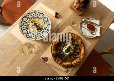 Genießen Sie eine köstliche Kombination aus Gourmet-Pizza mit frischen Zutaten und cremiger Pasta, perfekt präsentiert auf einem rustikalen Holztisch in A Stockfoto