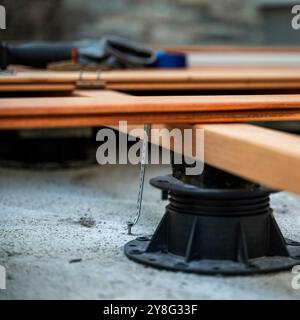 Eine detaillierte Aufnahme von Holzbalken auf verstellbaren Sockeln während des Decksbaus, gesichert durch Metallhalterungen. Die Werkzeuge liegen im Hintergrund und werden präsentiert Stockfoto