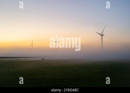 Malerische Aussicht auf Windturbinen, die während des Sonnenaufgangs über einer Nebelschicht aufsteigen Stockfoto