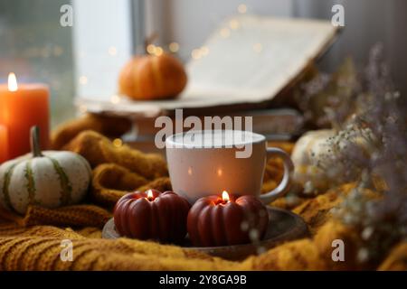 Tasse Kaffee und brennende Kerzen in Kürbisform auf weichem Pullover. Herbstatmosphäre Stockfoto