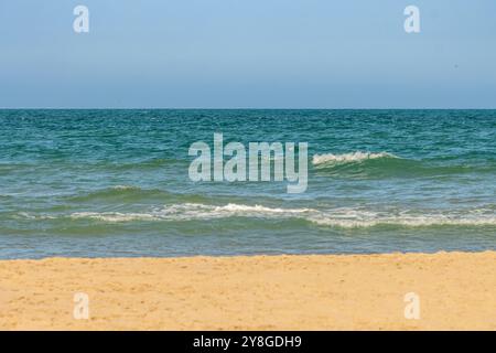 Dieses Bild zeigt eine ruhige Strandszene mit der Küstenlinie im Vordergrund, sanften Wellen in der Mitte und einem klaren blauen Himmel darüber. Stockfoto