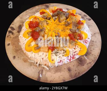 Eine hausgemachte Pizza mit gelben Paprika, Pilzen, Ananas, Tomatensauce und Kräutern auf einem Pizzastein. Stockfoto