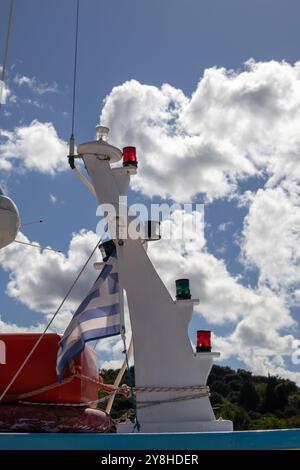 Das Boot hat in einem Hafen angedockt. Blick auf einen Mast mit Lichtern in verschiedenen Farben. Griechische Flagge. Blauer Himmel mit weißen Wolken. Astrakeri, Korfu, Griechenland. Stockfoto