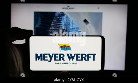 Person mit Mobiltelefon mit Logo der Schiffbaugesellschaft Meyer Werft GmbH Co. KG auf dem Bildschirm vor der Webseite. Schwerpunkt auf dem Display des Telefons. Stockfoto