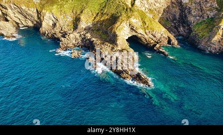 Blick aus der Vogelperspektive auf die felsige Küste mit klarem türkisfarbenem Wasser. Die Landschaft verfügt über zerklüftete Klippen und einen natürlichen Bogen, der durch Erosion geformt wurde. Kurven sanft cr Stockfoto