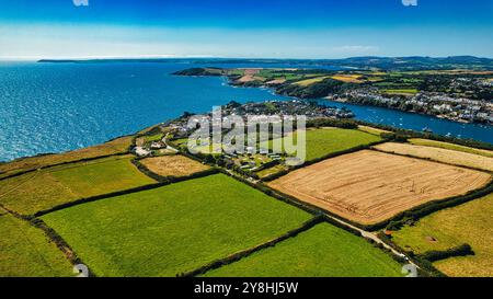 Blick aus der Vogelperspektive auf ein Küstendorf, umgeben von üppigen grünen Feldern und Ackerland. Das blaue Meer erstreckt sich im Hintergrund, mit Booten auf der Wa Stockfoto